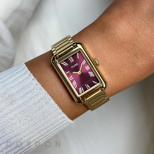 Reloj Cluse de mujer rectangular dorado con esfera vino puesto en la muñeca